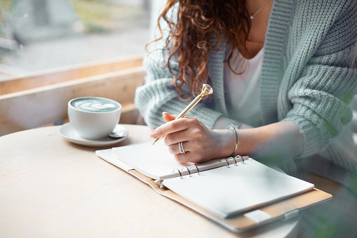 Woman holding a pen to take down notes with a cup of coffee beside her